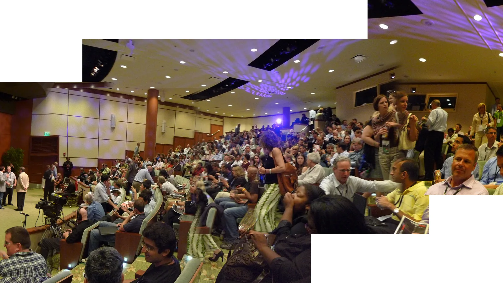 A speaker on a brightly lit conference stage addressing a large audience
